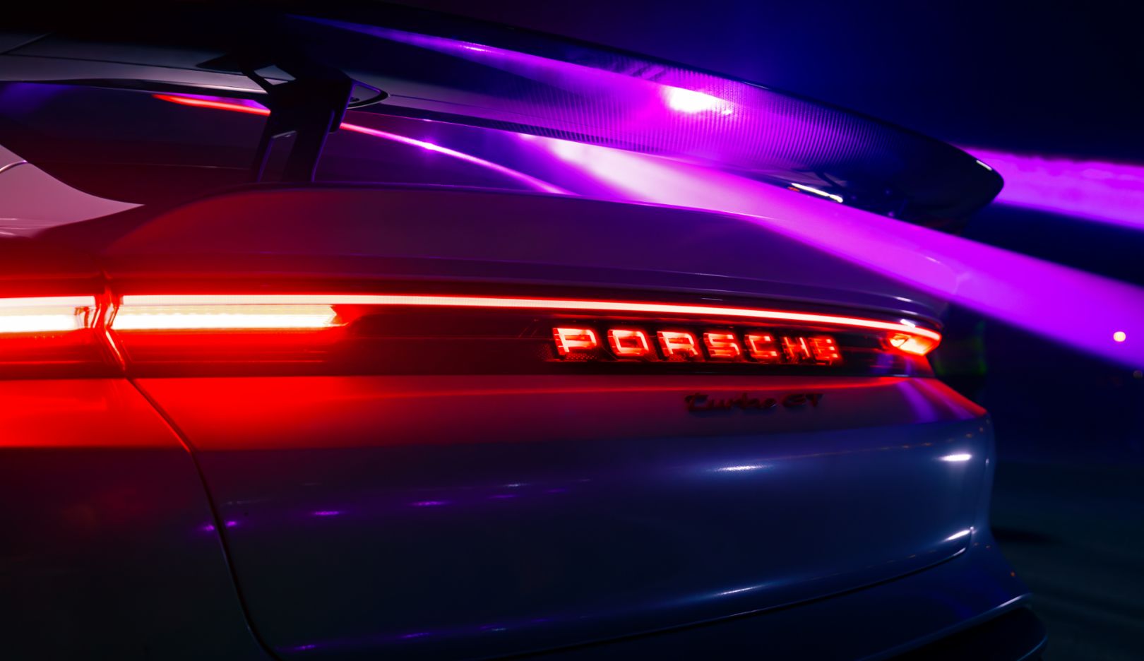 The details of the cars, such as the rear view of the Taycan Turbo GT, shine in the light of the backdrop.