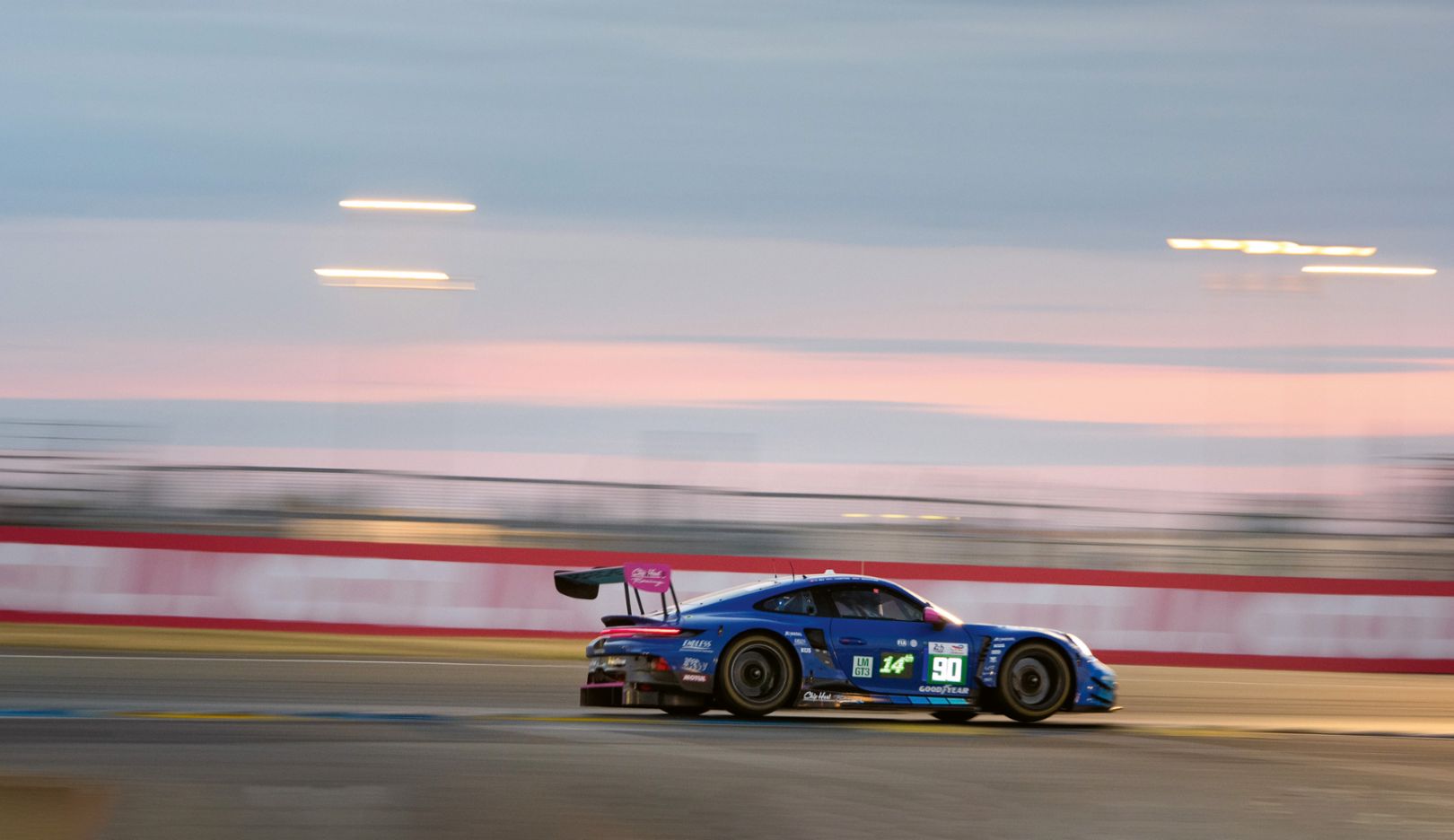 A dark blue race car with a distinctive rear wing and the starting number 90 speeds around a race track.