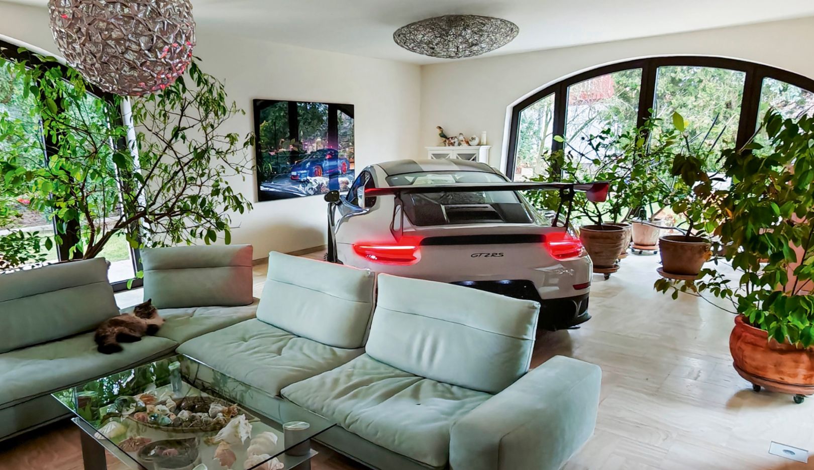 Ein Porsche 911 steht in einem stilvollen Wohnzimmer zwischen grünen Pflanzen und gemütlichen Möbeln. Die Mischung aus modernem Design und Automobil-Ikone macht den Raum einzigartig.