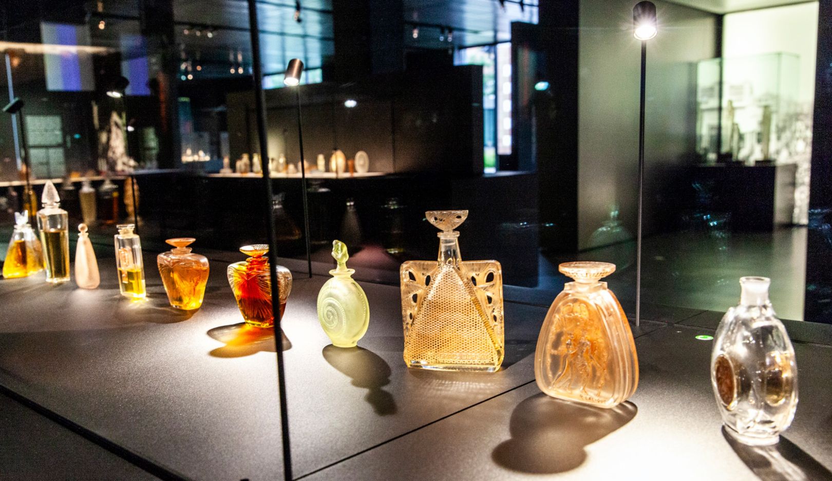 A view into this display case at the Musée Lalique in Wingen-sur-Moder. On the left, D'où vient-il from 1920, made for Vigny. Next to them are two prototypes from 1919. The fourth flacon was made for D'Héraud in 1914; the fifth and sixth bottles show butterfly metamorphoses. These are followed by the two models Le Succès and Grâce, made for D'Orsay, as well as L'Idylle and a prototype from 1910.