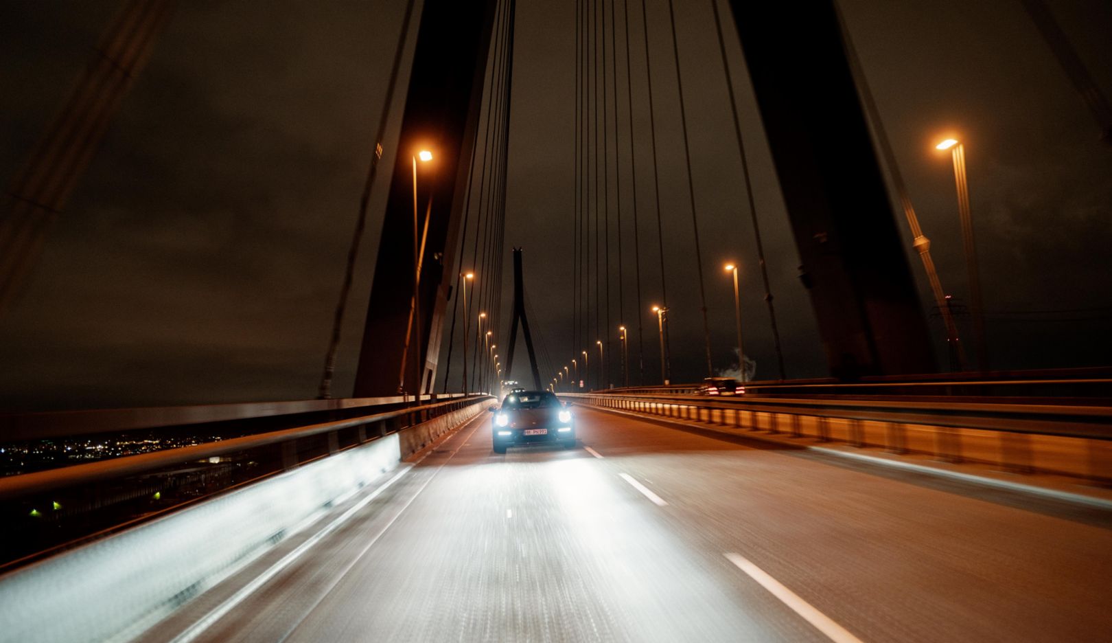 Kommt daher wie eine Filmszene: Der Porsche 911 Carrera 4S in Frontalansicht auf der Hamburger Köhlbrandbrücke bei Nacht.