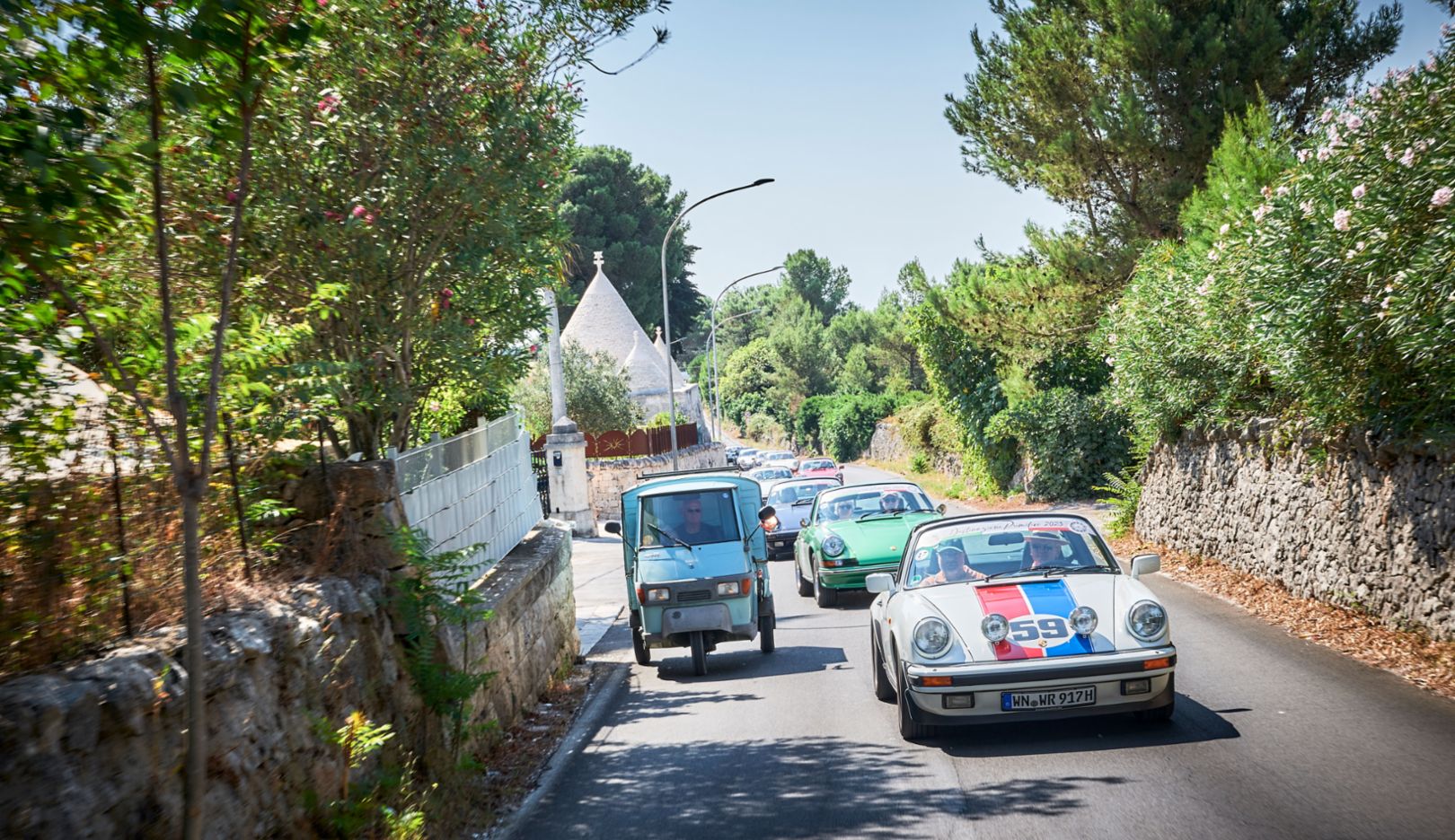 Todo un clásico: en el viaje a Martina Franca por la llanura del Valle d'Itria, un Piaggio Ape de tres ruedas adelanta al convoy de Porsche