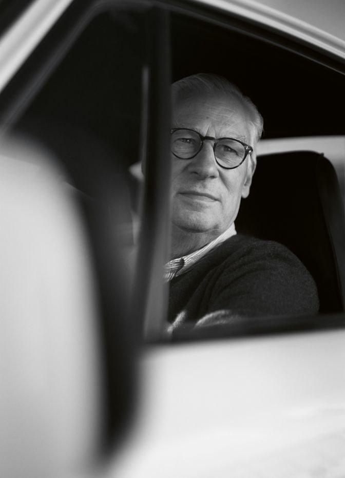 Ein Mann mit Brille sitzt im Auto und blickt aus dem Fenster, während sanftes Licht sein Gesicht erleuchtet.