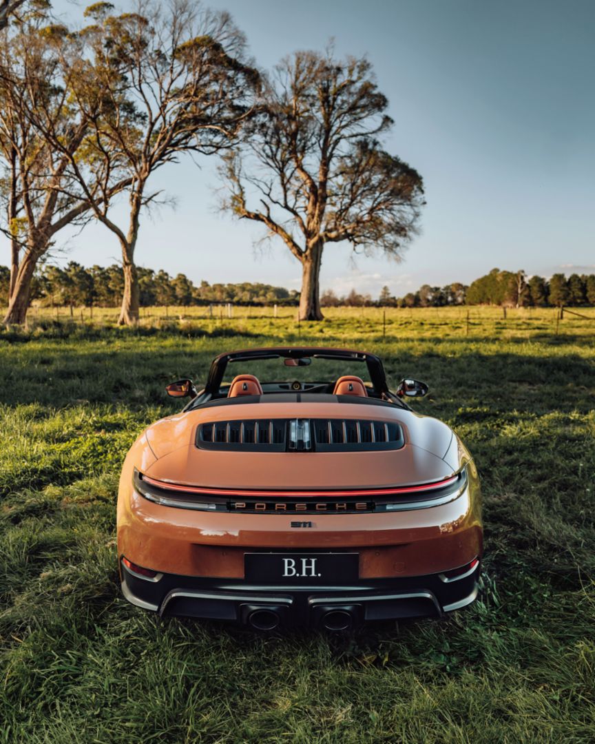 A Porsche 911 Turbo is parked on a driveway in front of a white modern building with large windows and palm trees in the background.