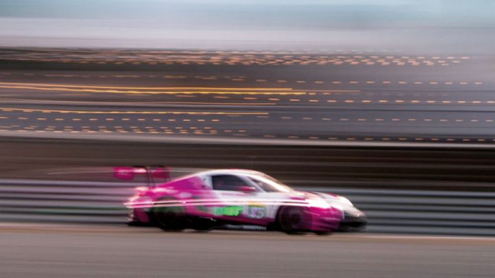 Two men lean against red Porsche sports cars in an industrial hall, parked side by side.
