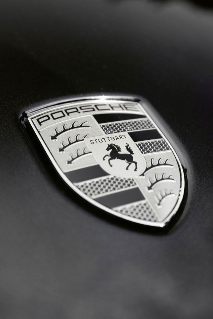 Eine Nahaufnahme des Porsche-Wappens auf der Motorhaube eines Autos, welche das ikonische Schilddesign und das Pferdelogo zeigt.