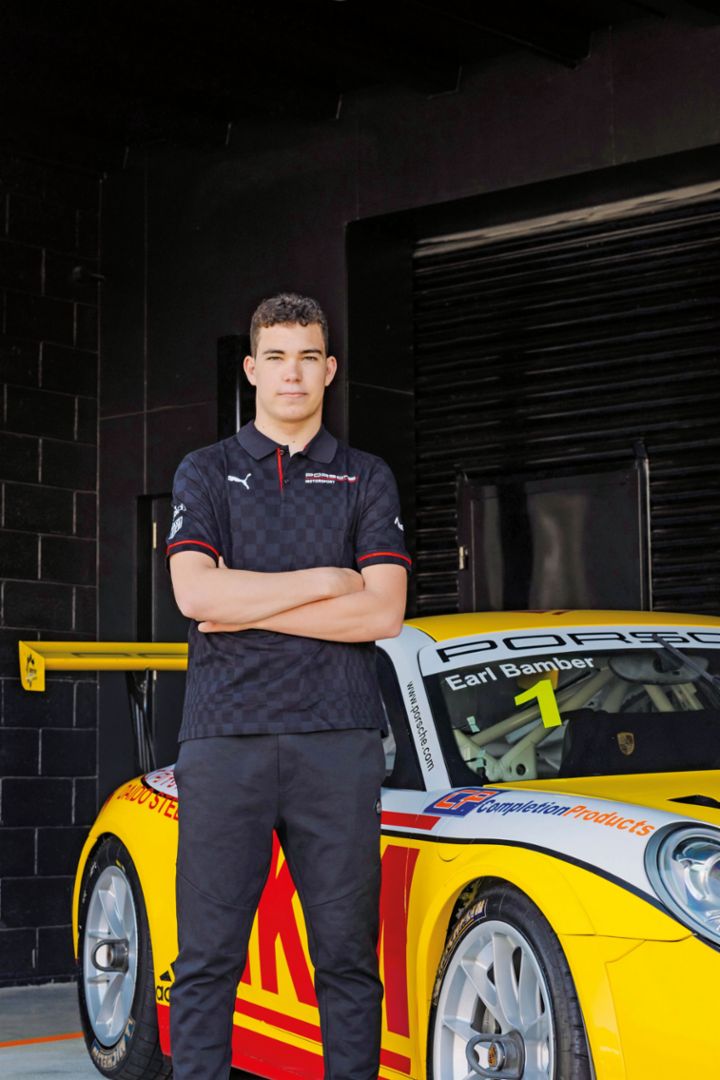 A young man in a Porsche Polo shirt to a red and yellow Porsche 911 race car. 