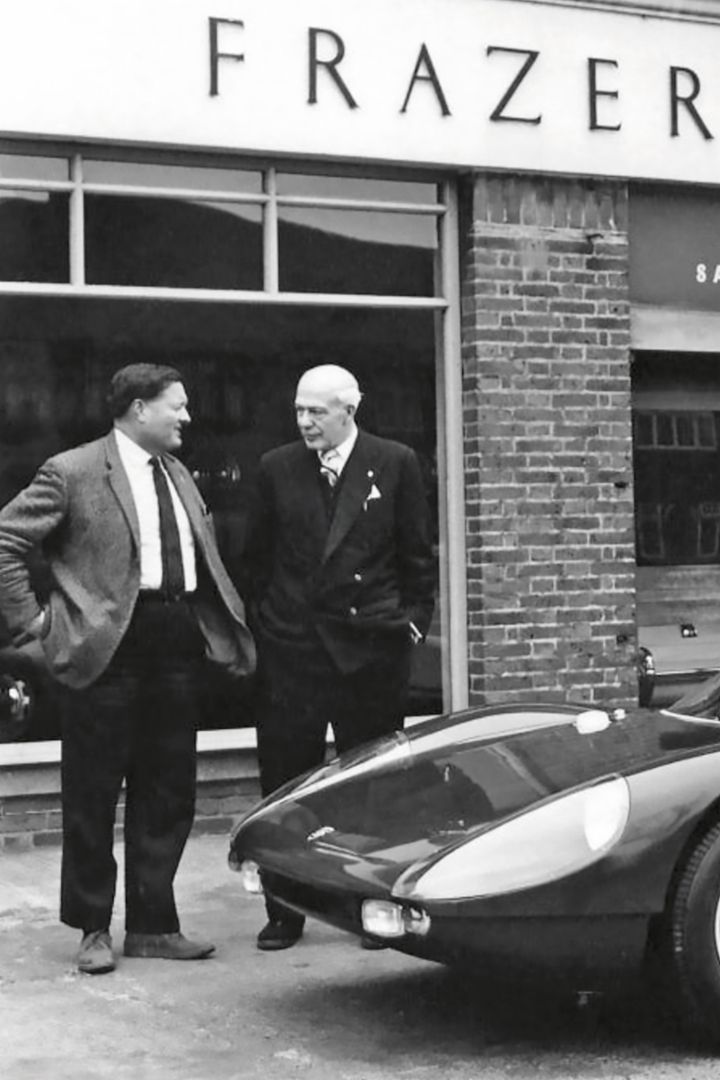 A woman stands smiling next to a Porsche 924, with the sun shining in the blue sky and the surroundings bathed in sunlight