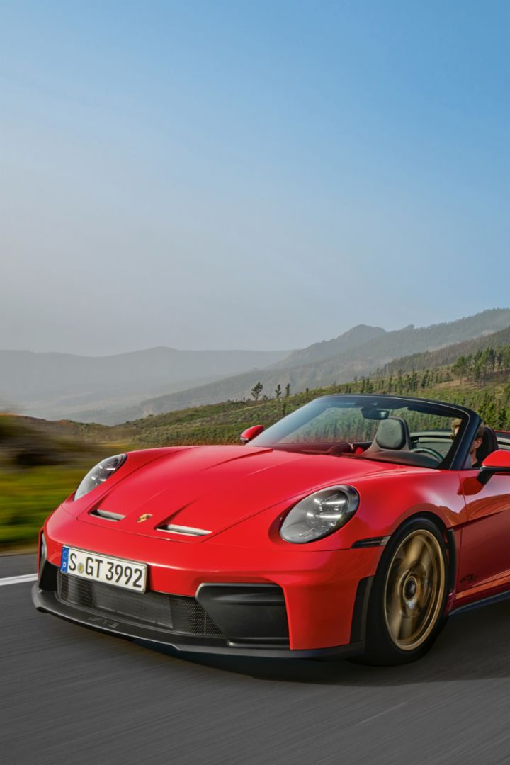 Three people stand beside three Porsche vehicles on a large paved surface.