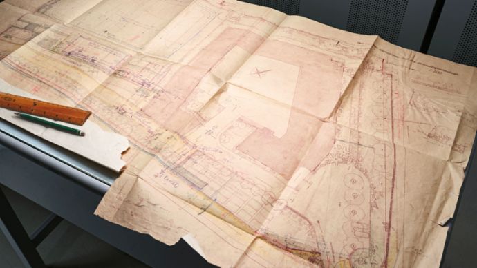An old plan lies on a table, surrounded by a ruler and in an archive room.
