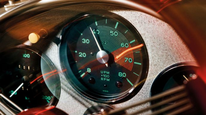 A classic vehicle dashboard shows illuminated gauges with a prominently highlighted RPM mark.
