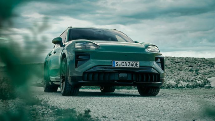 A green SUV is parked on a gravel track in an open landscape beneath heavy cloud cover.