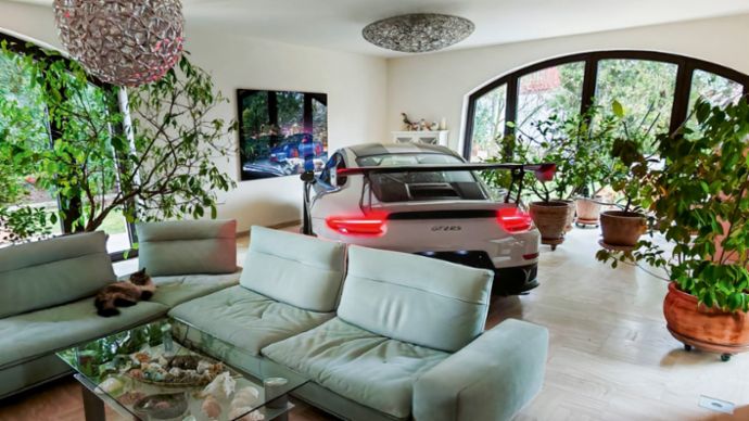Ein Porsche 911 steht in einem stilvollen Wohnzimmer zwischen grünen Pflanzen und gemütlichen Möbeln. Die Mischung aus modernem Design und Automobil-Ikone macht den Raum einzigartig.