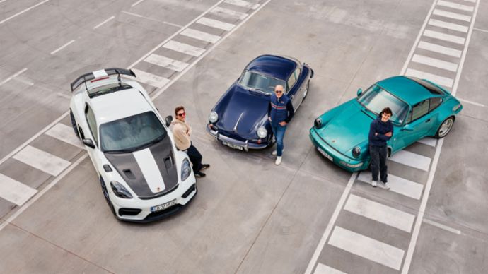 Three people stand beside three Porsche vehicles on a large paved surface.