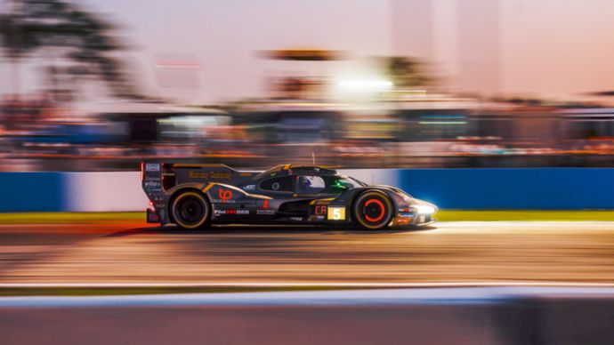A race car speeds along a racetrack at dusk.