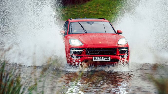 A red SUV drives through a water crossing, creating large splashes.