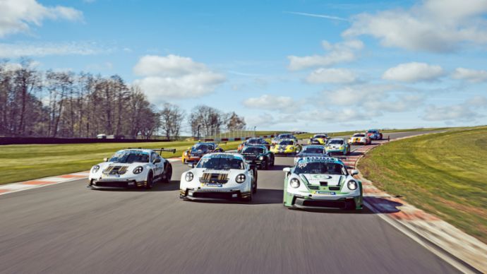 Multiple race cars drive closely together through a corner on a racetrack.