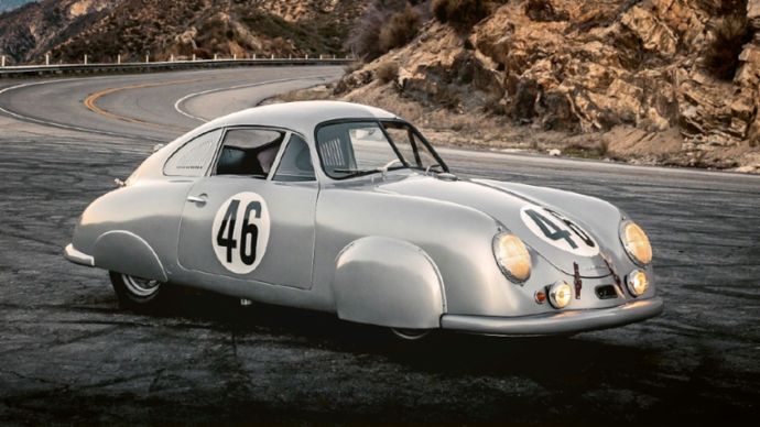 Ein historischer Porsche steht auf einer kurvigen Bergstraße vor einer Felslandschaft bei Sonnenuntergang.