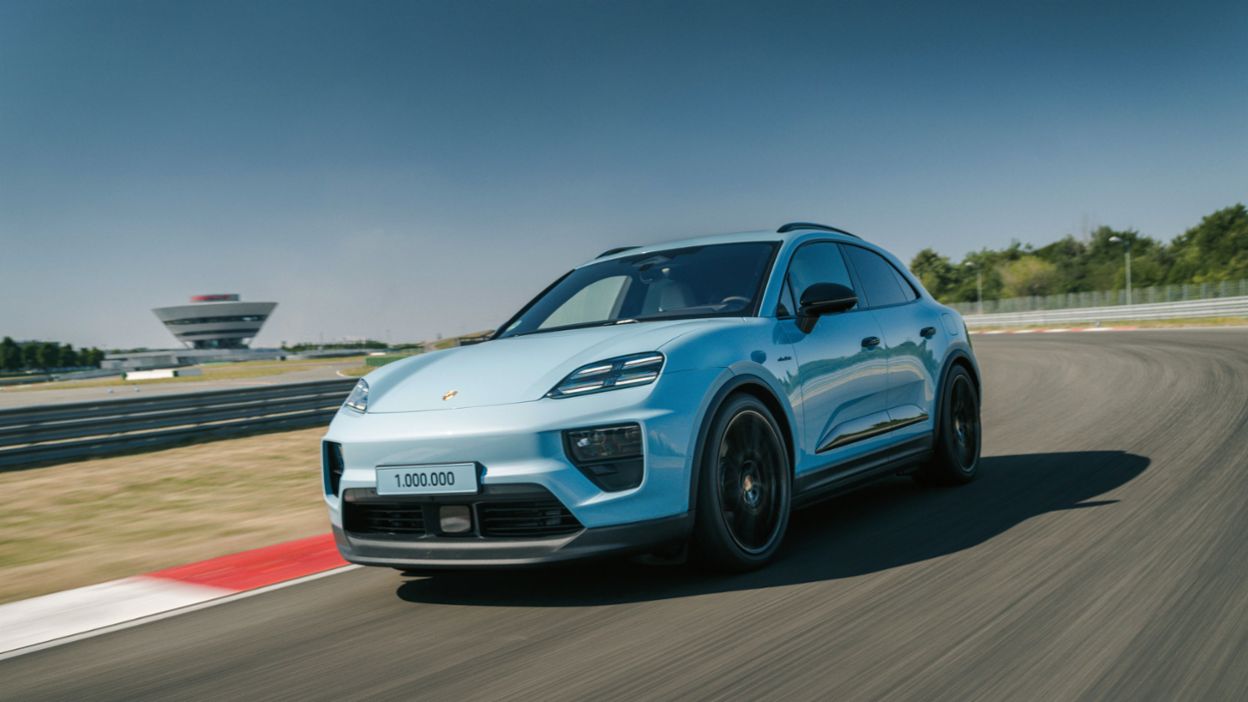 Ein Porsche Macan fährt auf einer Rennstrecke mit einem markanten Aussichtsturm im Hintergrund und einer „1.000.000“-Plakette auf der Fahrzeugfront.