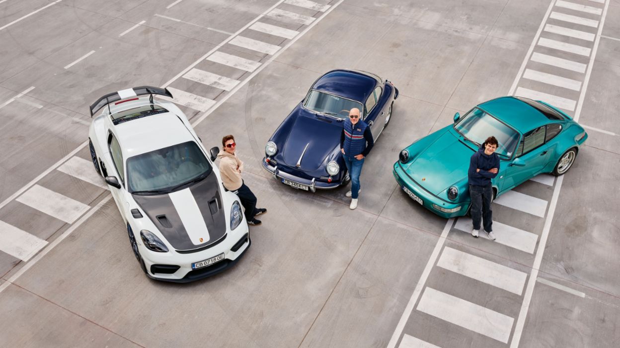 Three people stand beside three Porsche vehicles on a large paved surface.