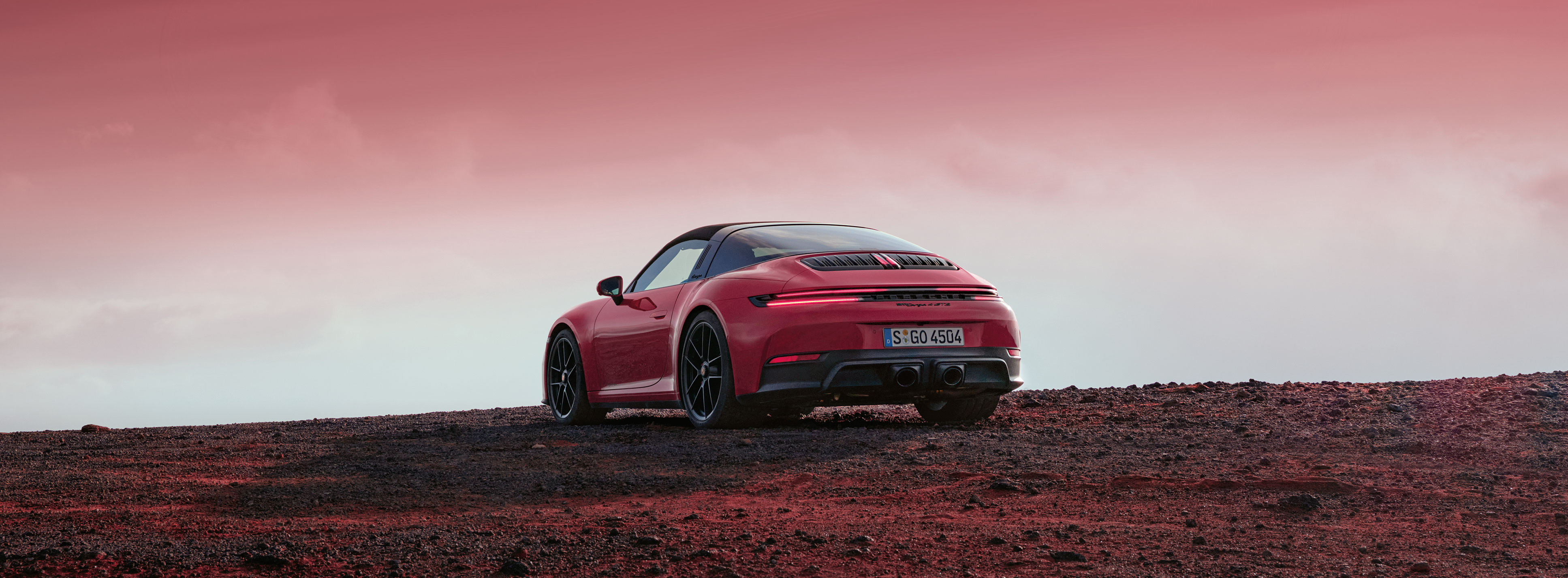 Ein Porsche 911 steht auf einer kargen, roten Landschaft unter einem dramatischen, karminroten Himmel. 