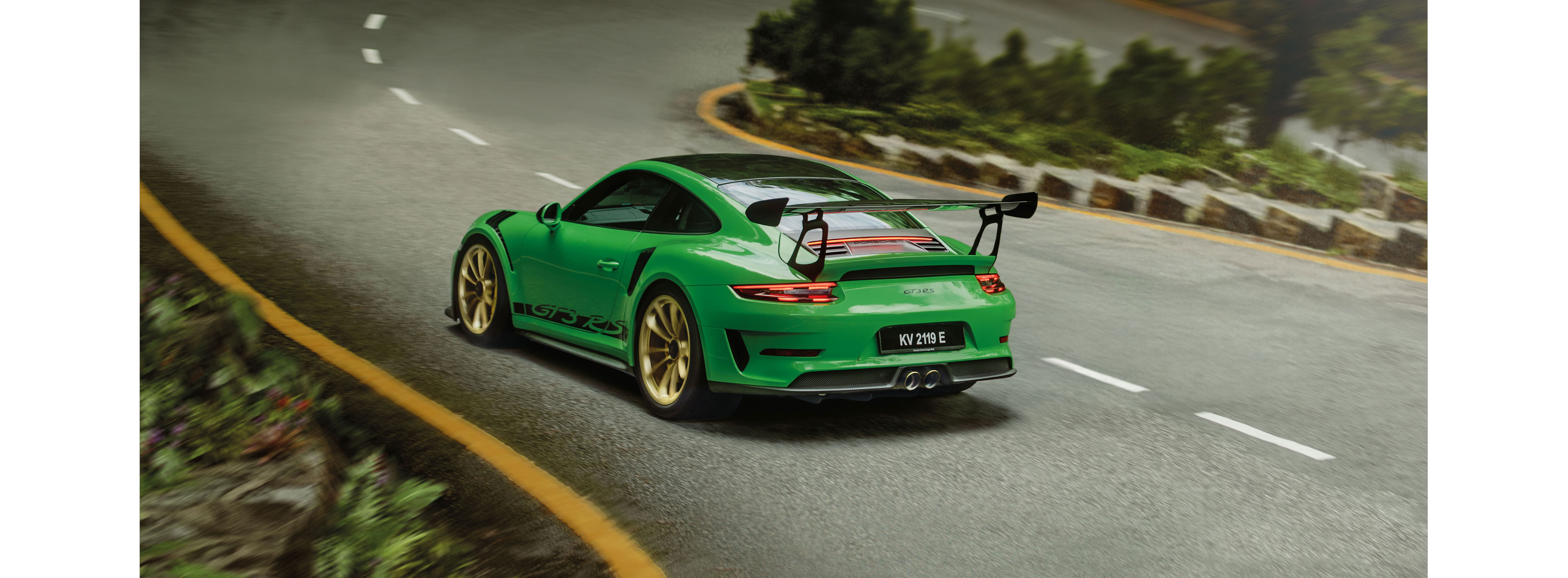 A green Porsche 911 GT3 RS speeds through a winding road in the forest.